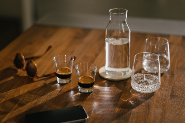 Nahaufnahme eines Holztisches mit Gläsern, Wasser und Espresso